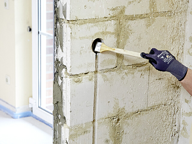 Nahaufnahme, wie mit einem Flachpinsel die Öffnung für die Unterputzdose in der Wand vorgenässt wird.