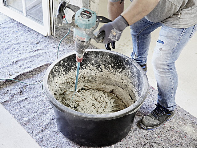 Blick in einen Eimer, in dem eine Person mit einem Rührgerät Kalkzement-Putz anrührt