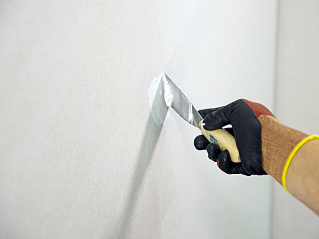 Aufnahme einer Hand, die mit einem Spachtel den Malerspachtel auf ein Loch in der Wand aufträgt