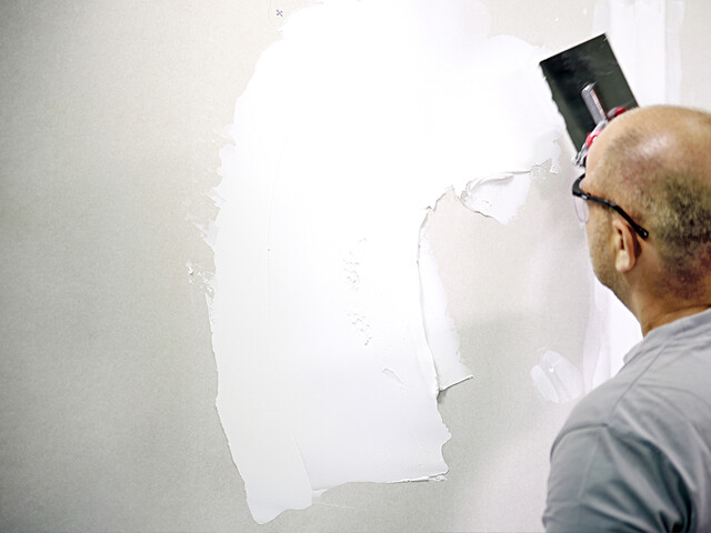 Nahaufnahme eines Mannes, der eine Wand mit dem Malerspachtel verspachtelt