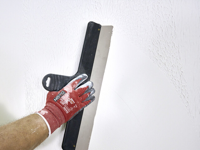 Nahaufnahme auf eine Wand, welche mit einem breiten Flächenspachtel glatt abgezogen wird