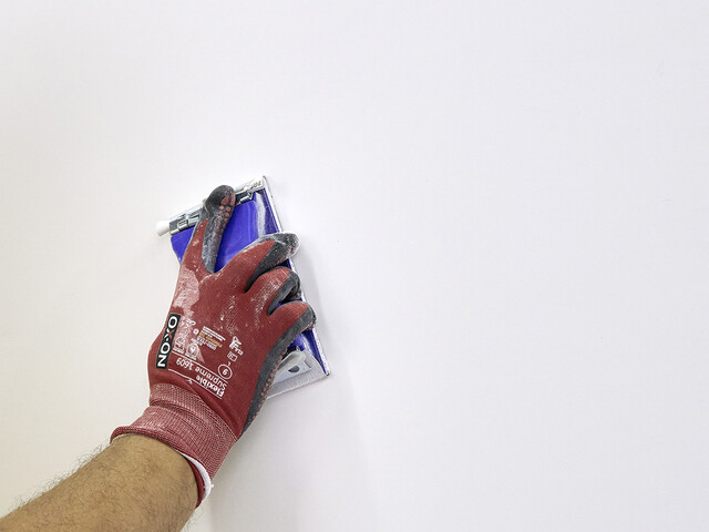 Nahaufnahme auf eine Wand, welche mit einem blauen Handschleifer abgeschliffen wird