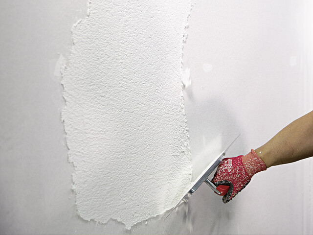 Aufnahme einer Hand, die mit einem Glätter Scheibenputz auf eine Wand aufträgt