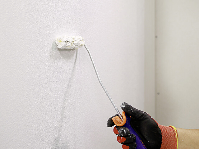 Nahaufnahme, wie eine Hand mit einer Malerrolle eine Grundierung auf eine Wand aufgetragen wird