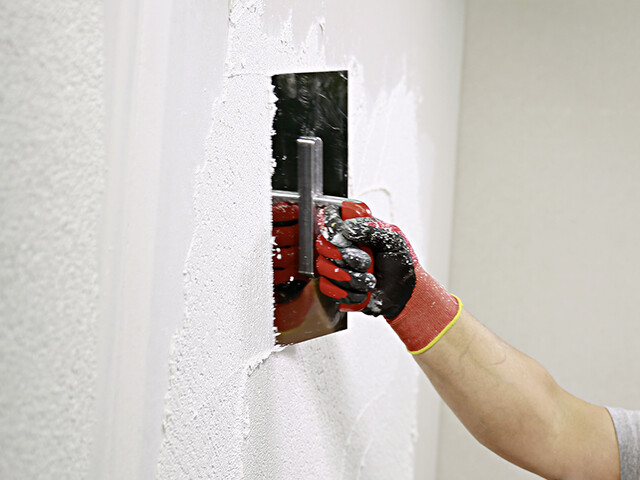 Nahaufnahme auf eine Hand, die mit einem Glätter eine Wand mit dem Münchner Rauputz verputzt