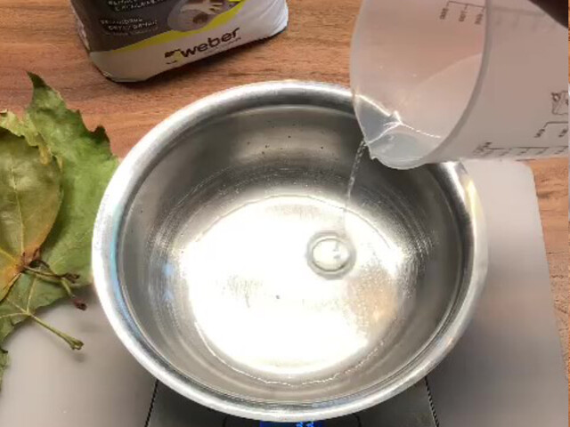 Nahaufnahme, wie Wasser aus einem Messbecher in eine Metallschale gegossen wird