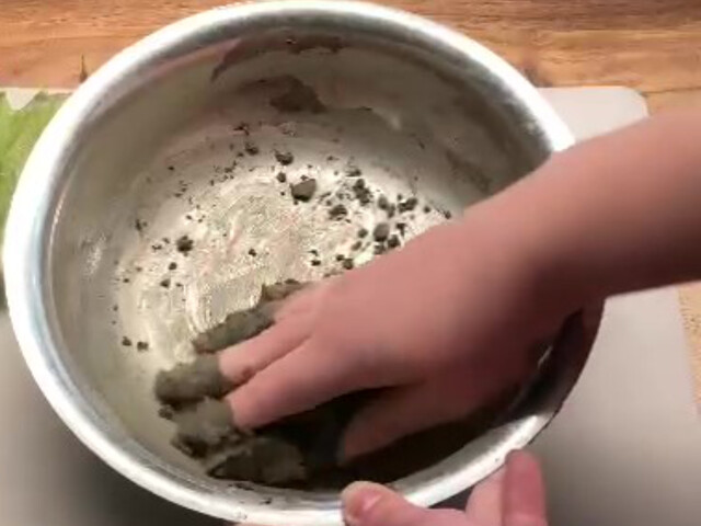 Nahaufnahme, wie der Bastelbeton mit einer Hand in einer Metallschale geknetet wird, während eine zweite Hand die Schale festhält