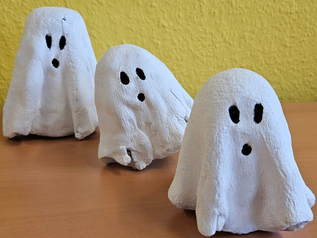 Aufnahme von drei weiß bemalten Geistern aus Bastelbeton mit schwarzen Augen und Mund hintereinander.